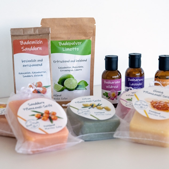 Labels op verschillende cosmetische producten: Doypacks met badmelk en badpoeder, bruine glazen flessen met badaroma, evenals plantaardige zeep met ronde etiketten in doorzichtige zakken, op een lichte achtergrond.
