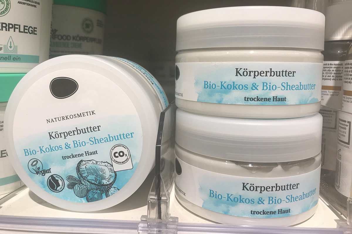 Witte crèmepot met natuurlijke cosmetica lichaamsboter op de plank, gelabeld op de deksel en het lichaam met kleurrijk bedrukte etiketten in blauw-wit.