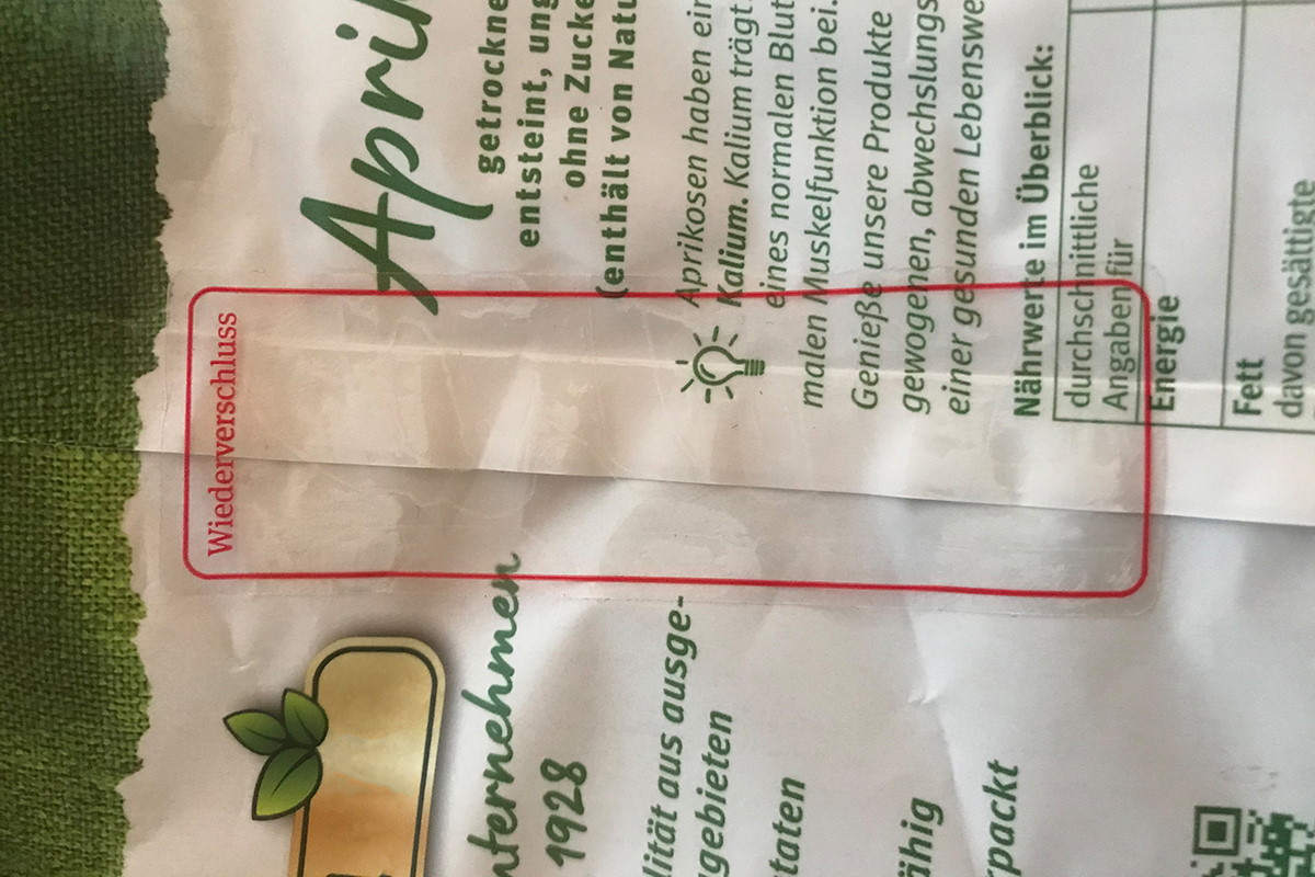 Sluitstickers: transparante herbruikbare sticker, bedrukt met een gekleurd kader en de tekst Herverpakking, op een zakverpakking met abrikozen.