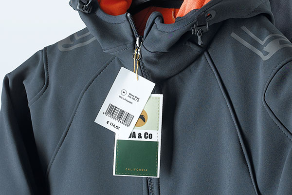 Kleurig bedrukte hangtags met prijs- en productinformatie, aan een grijze softshell jas.