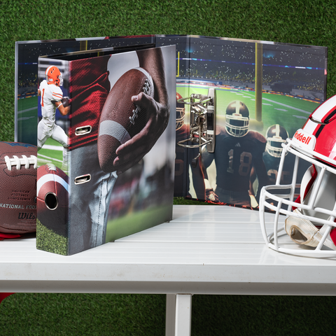 Ein Ordner mit Football-Motiven, ein Football und ein Helm auf einem Tisch, umgeben von grünem Rasen.