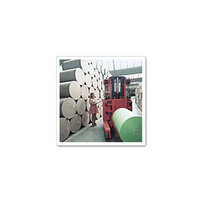 Een vrouw bedient een heftruck in een magazijn om grote papierrollen te verplaatsen, terwijl er op de achtergrond nog meer rollen gestapeld zijn.