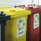 Drei Mülltonnen in verschiedenen Farben für die getrennte Abfallentsorgung: Gelb für Plastik, Rot für Glas und Schwarz für Restmüll.
