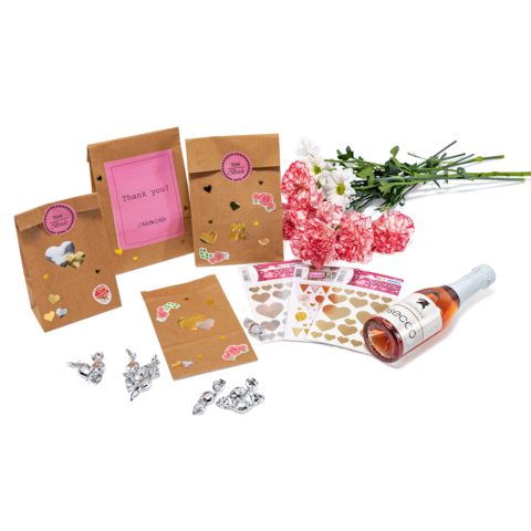 Geschenktüten mit Aufklebern, eine Flasche Roséwein, Blumen und Herzaufkleber auf einem Tisch arrangiert.