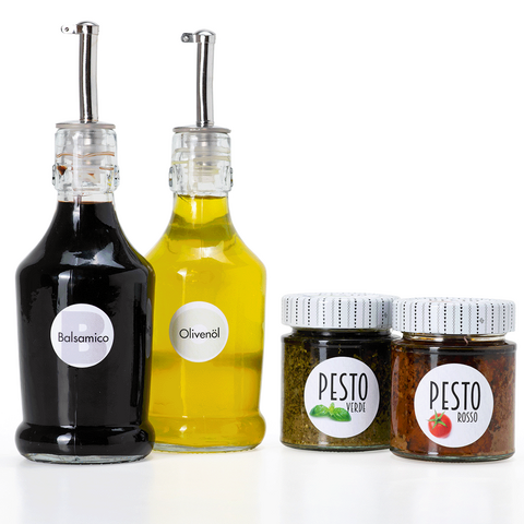 Twee flessen balsamico en olijfolie, evenals twee glazen pesto in verschillende smaken, op een witte achtergrond.