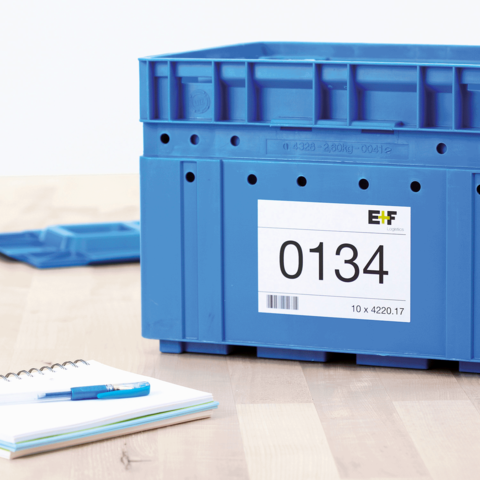 Blaue Kunststoffbox mit der Nummer 0134 und einem Etikett, daneben ein Notizblock und ein blauer Stift auf einem Tisch.