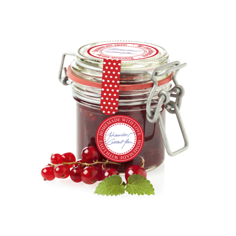 Ein Glas selbstgemachte Johannisbeermarmelade mit einem roten Etikett und frischen Johannisbeeren daneben.