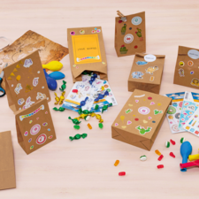Felgekleurde cadeautjeszakken en knutselmaterialen op een tafel, waaronder stickers, ballonnen, scharen en snoepjes.