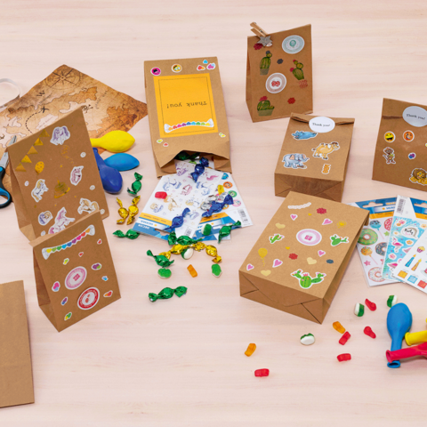 Felgekleurde cadeautjeszakken en knutselmaterialen op een tafel, waaronder stickers, ballonnen, scharen en snoepjes.