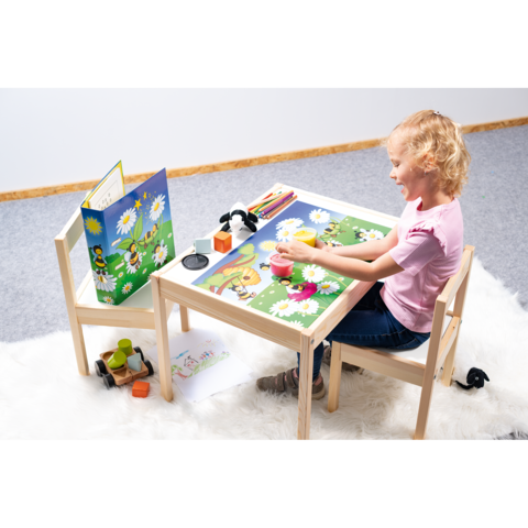 Ein Mädchen sitzt an einem Tisch und spielt mit bunten Spielzeugen und einem Puzzle, umgeben von einer fröhlichen, blühenden Landschaft.