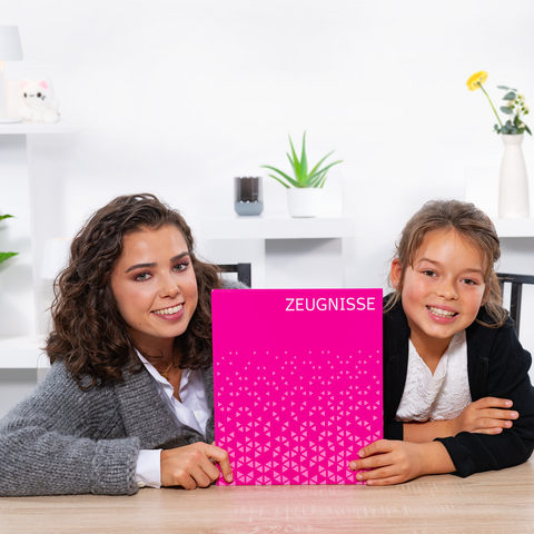 Twee meisjes zitten aan een tafel en houden een roze schrift met de opdruk 'GETUIGENISSEN'. Ze glimlachen naar de camera.
