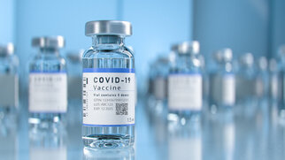 COVID-19-vaccinfles met etiket dat belangrijke informatie zoals batchnummer en vervaldatum bevat, voor onscherpe andere flessen.