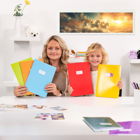 Een vrouw en een kind zitten aan een tafel, houden kleurrijke mappen in hun handen en glimlachen. Op de tafel liggen foto's.