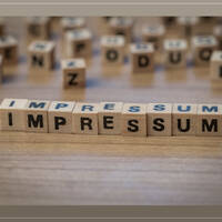 Houten letters vormen het woord "IMPRESSUM" op een tafel, omringd door andere letters.