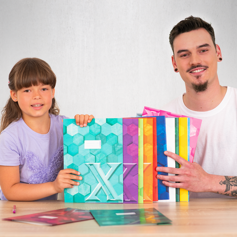 Ein Kind und ein Erwachsener halten bunte, geometrische Muster und Bücher in der Hand, während sie an einem Tisch sitzen.