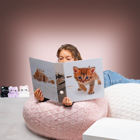 Een kind zit in een grote, ronde zitzak en leest een map met een afbeelding van een kitten op de voorkant.