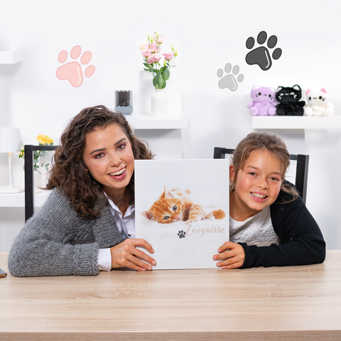 Een vrouw en een meisje houden een boek met een kattenomslag vast terwijl ze aan een tafel zitten. Op de achtergrond zijn decoratieve elementen zichtbaar.