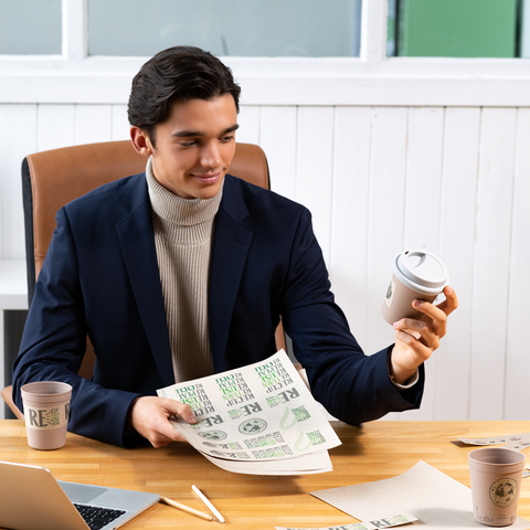 Een jonge man in een pak houdt een koffiebeker en een vel papier met tekst vast in een kantooromgeving.
