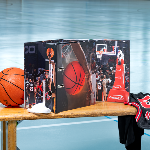 Ein Basketball liegt auf einem Tisch neben einem Ordner mit Basketballmotiven und einem Basketballtrikot.