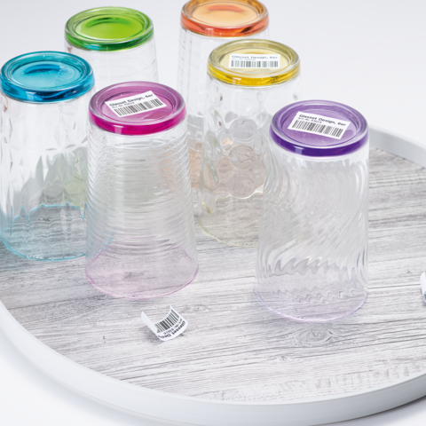 Fünf bunte Gläser mit verschiedenen Deckeln auf einem runden Tablett. Die Gläser sind transparent und haben unterschiedliche Muster.