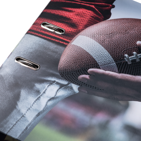 Ein Football wird von einer Hand gehalten, während ein Teil eines roten Trikots und einer grauen Hose sichtbar ist.