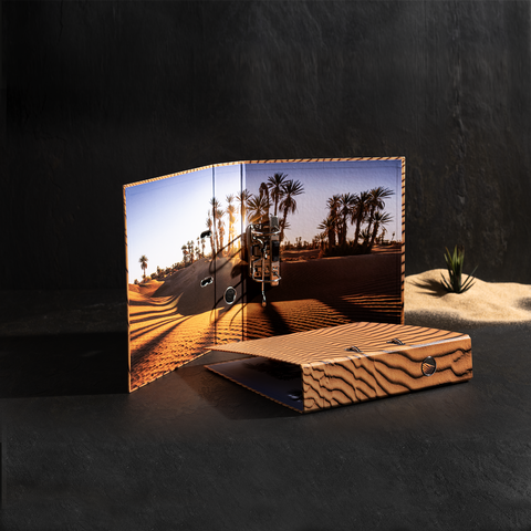 Ein aufgeschlagenes Notizbuch mit einem Bild von Palmen und Sanddünen im Sonnenlicht. Der Einband hat ein Holzmaserungsdesign.