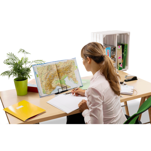 Eine Person sitzt an einem Schreibtisch, betrachtet eine Landkarte und macht Notizen in ein Notizbuch. Pflanzen und Ordner sind im Hintergrund sichtbar.