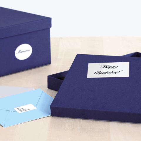 Eine geöffnete, dunkelblaue Geschenkbox mit der Aufschrift "Happy Birthday!" und zwei Umschlägen in verschiedenen Farben auf einem Tisch.