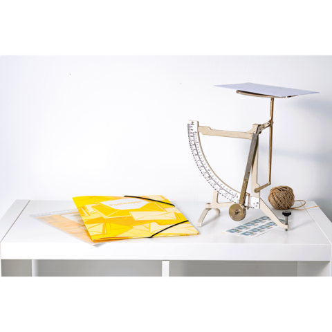 Ein Tisch mit einer Waage, gelben Ordnern, einem Notizblock und einer Schnurrolle.