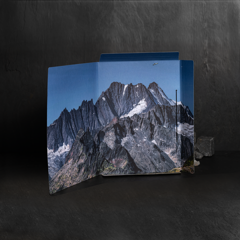 Ein aufgeschlagenes Faltblatt zeigt eine beeindruckende Berglandschaft mit schroffen Gipfeln und schneebedeckten Bereichen.