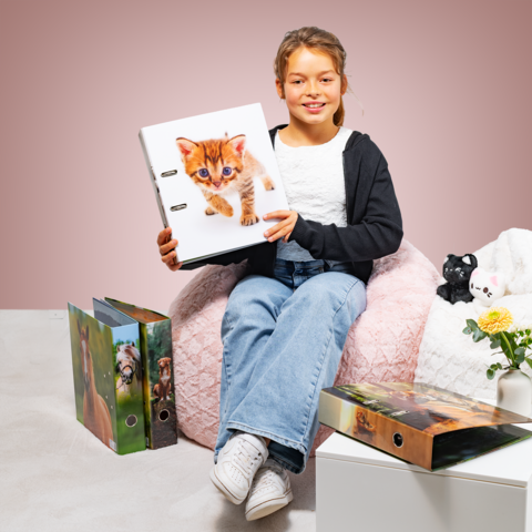 Een meisje zit op een zitzak en houdt een map vast met een kitten op de omslag. Om haar heen staan nog meer mappen en een plant.