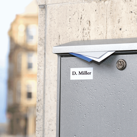 Graue Briefkasten mit dem Namen "D. Miller" auf einem urbanen Hintergrund, leicht feucht von Regen.