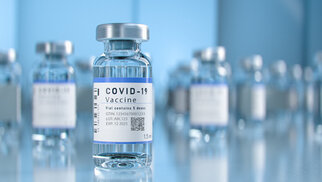 COVID-19-vaccinflacons op een tafel, met een heldere vloeistof en een etiket dat belangrijke informatie bevat.