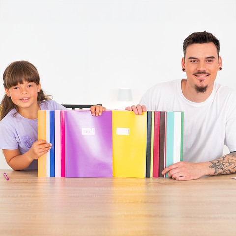 Ein Kind und ein Erwachsener sitzen an einem Tisch und halten bunte Ordner. Der Tisch ist leer, und sie schauen in die Kamera.