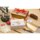 Geschenkverpackungen in Gold und Weiß mit Punkten, umgeben von Dekorationen wie Kerzen, Tannenzapfen und Geschenkband auf einem Holztisch.
