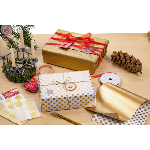 Geschenkverpackungen in Gold und Weiß mit Punkten, umgeben von Dekorationen wie Kerzen, Tannenzapfen und Geschenkband auf einem Holztisch.