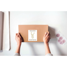 Hände halten ein braunes Paket mit einem Aufkleber, der "Frohe Weihnachten und ein glückliches neues Jahr" zeigt.