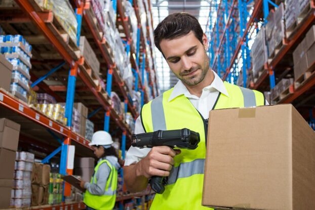 Logistiekmedewerker die een verzendlabel op een doos scant, in het magazijn, liggend formaat.