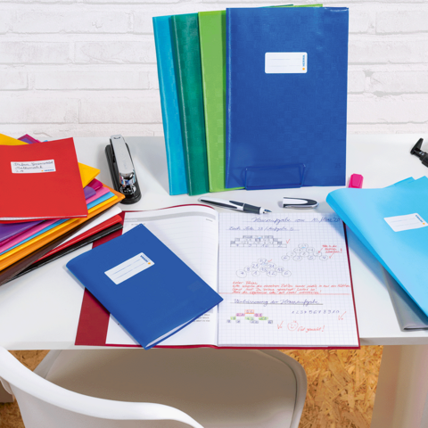 Eine Frau und ein kleines Mädchen sitzen an einem Tisch und blättern durch ein Notizbuch. Bunte Stifte und ein Ordner liegen auf dem Tisch.