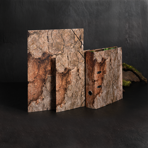 Drei Ordner mit einer Holzrinde-Optik stehen auf einer dunklen Oberfläche. Der größte Ordner hat eine Lochstanzung.