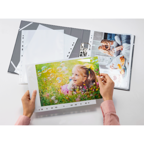 Eine Person hält ein Foto eines lächelnden Mädchens in einer bunten Umgebung, während ein Fotoalbum mit weiteren Bildern geöffnet ist.