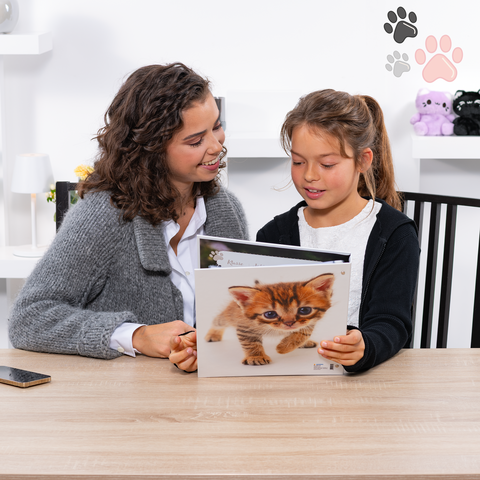 Een vrouw en een meisje zitten aan een tafel en bekijken samen een boek met afbeeldingen van katten.
