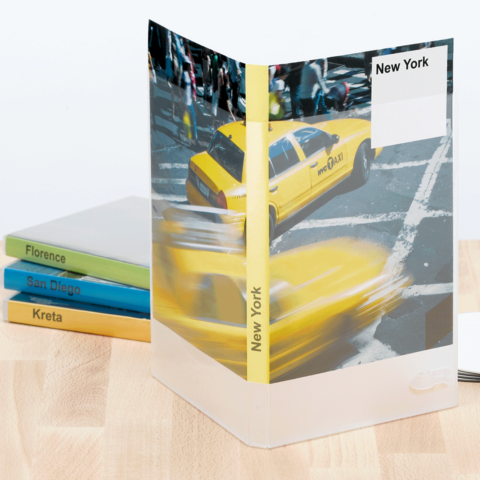 Gelbes Taxi auf einer Straße in New York, umgeben von einem transparenten Ordner mit dem Schriftzug "New York". Im Hintergrund sind farbige Buchrücken sichtbar.