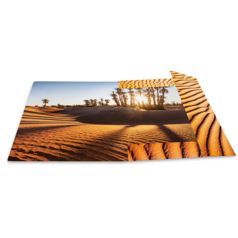 Sanddünen mit Palmen im Hintergrund, beleuchtet von der Sonne, die durch die Wolken scheint.