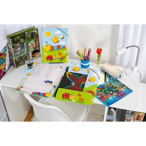 Ein Schreibtisch mit bunten Schulmaterialien, darunter Notizhefte, Stifte, eine Lampe und eine Vase mit einer Blume.