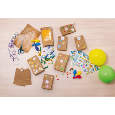 Bastelmaterialien auf einem Tisch, darunter Papiertüten, Aufkleber, Scheren, Bänder, Luftballons und bunte Bastelutensilien.