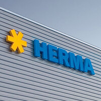 Geel sterrenlogo's en blauwe letters vormen het woord 'HERMA' op de buitenmuur van een modern gebouw.