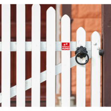 Weißer Gartenzaun mit einem roten Schild, das auf einen Hund hinweist. Der Zaun hat einen runden Türknauf.