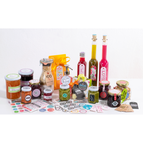 Verschiedene Gläser mit Marmelade, Ölen und Gewürzen, dekoriert mit bunten Etiketten und Verpackungen auf einem Tisch.