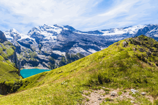 Panoramisch uitzicht op groene heuvels en besneeuwde bergen, omringd door helder water en een blauwe lucht.